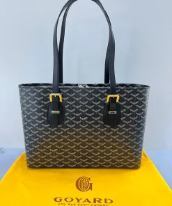 Full view of a spacious tote bag with a signature green geometric pattern (Goyard style), white stitching, and adjustable buckle details, standing on a branded dust bag.