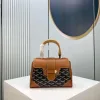 Front view of a rigid, structured handbag (Goyard Saïgon style) featuring a signature chevron/Y-pattern, wooden top handle, and corner reinforcements.