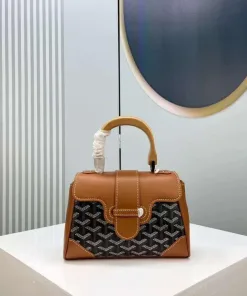 Front view of a rigid, structured handbag (Goyard Saïgon style) featuring a signature chevron/Y-pattern, wooden top handle, and corner reinforcements.