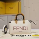 Close-up of white Fendi Roma Double Handle mini bag with tortoiseshell handle, gold hardware, and detachable shoulder strap on a shelf with Fendi boxes.