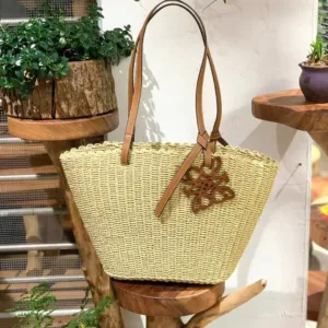 Full view of the handwoven basket bag with leather trim, featuring the distinctive Anagram logo patch on the front.