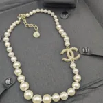 High-angle shot of a classic faux pearl necklace with a dazzling crystal-studded CC logo pendant, displayed with matching logo stud earrings on a black garment.