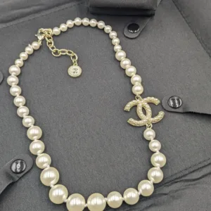 High-angle shot of a classic faux pearl necklace with a dazzling crystal-studded CC logo pendant, displayed with matching logo stud earrings on a black garment.