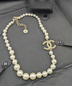 High-angle shot of a classic faux pearl necklace with a dazzling crystal-studded CC logo pendant, displayed with matching logo stud earrings on a black garment.