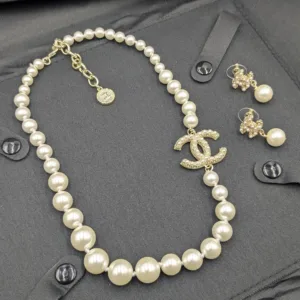 Overhead product image of the full matching set, including the gold-tone, crystal-embellished CC earrings standing next to the long pearl necklace.