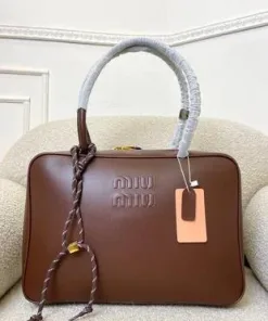A Miu Miu leather tote bag with embossed logo and braided handle detail placed on a cushioned chair.