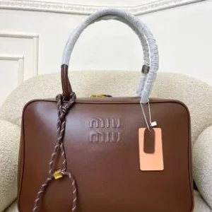 A Miu Miu leather tote bag with embossed logo and braided handle detail placed on a cushioned chair.