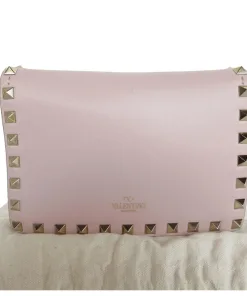 Close-up front view of light pink Valentino Garavani Rockstud leather shoulder bag with gold-tone pyramid studs and logo stamp.