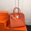 Full front view of the larger orange pebbled leather tote bag with open top and gold/silver metal hardware.