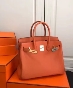 Full front view of the larger orange pebbled leather tote bag with open top and gold/silver metal hardware.