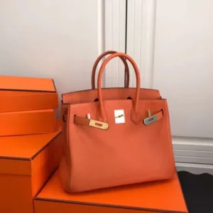 Full front view of the larger orange pebbled leather tote bag with open top and gold/silver metal hardware.