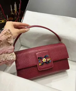 Red textured leather baguette shoulder bag featuring a multi-colored jeweled floral buckle detail, held by a hand.