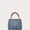Front view of the Small Valentino Garavani Roman Stud Handle Bag in quilted denim with contrasting stitching and antique brass maxi studs.