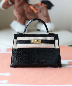 Close-up of shiny, structured mini crocodile handbag with gold-tone turn-lock hardware and top handle, resting in a white box.