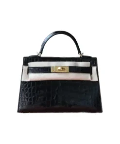 Close-up of shiny, structured mini crocodile handbag with gold-tone turn-lock hardware and top handle, resting in a white box.