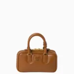 Close-up of a Miu Miu mini leather box handbag featuring gold zippers and top handles.